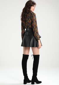 Blouse sombre à fleurs coupée, à manches longues, associée à une jupe évasée en faux cuir noir et des bottes en suède noir au-dessus du genou.