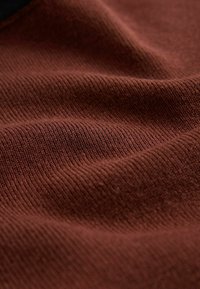 Hnedá rebrovaná tkanina s mäkkou textúrou, ktorá zobrazuje jemné variácie odtieňov a hladký, rovnomerný vzor pletenia po celom povrchu.