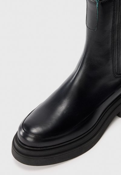 Stivaletto in pelle nera con punta tonda, caratterizzato da una finitura liscia e una spessa suola in gomma nera. Presenta dettagli turchesi sulla cerniera.