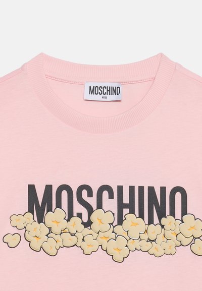 Ροζ μπλουζάκι για νήπια με μαύρο κείμενο "MOSCHINO" και σχέδια καρτούν με ποπ κορν κάτω από την ετικέτα στο λαιμό που γράφει "MOSCHINO KID."