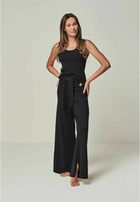 Schwarzes, geripptes Tanktop kombiniert mit schwarzen, weit geschnittenen Hosen, die eine vordere Schlaufenbindung und Schlitze am Saum haben. Glatte Textur, minimalistisches Design.