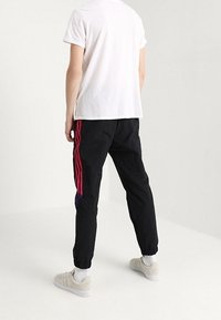 Černé joggingové kalhoty s růžovými pruhy, elastickými manžetami a kontrastním fialovým akcentem. V kombinaci s bílým tričkem a světlými teniskami.