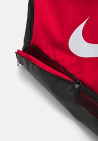 Rode en zwarte rugzak met een opvallend wit logo, een ritsvak en mesh accenten, gemaakt van duurzaam stof met een gestructureerde afwerking.