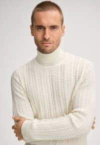 Gebreide turtleneck sweater in off-white met een kabelpatroon, voorzien van geribbelde manchetten en een textuurafwerking.