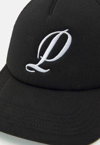 Black cap made of fabric with a curved brim. Features a white embroidered letter "P" on the front. Visible stitching along the brim.