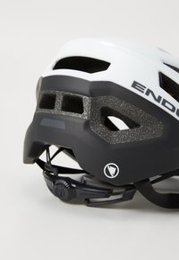 Eine Nahaufnahme eines weißen und schwarzen Fahrradhelms mit Belüftungsöffnungen und einem verstellbaren Riemen, mit sichtbarem Logo an der Seite.