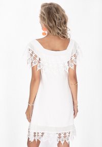 Rochie albă cu o croială lejeră, accente din dantelă pe umeri și la tiv, și un material texturat cu un model punctat.