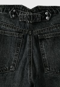Dos d'un jean en denim noir montrant deux poches, passants de ceinture, une boucle rectangulaire en métal et des rivets sur la ceinture.