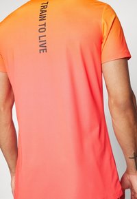 Camiseta deportiva de manga corta en un degradado de naranja y rosa, con una textura suave y el texto "TRAIN TO LIVE" en negro en la parte posterior.