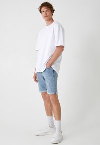 Biała, oversize'owa koszulka, jasne dżinsowe szorty z podwiniętymi mankietami, białe sneakersy i prążkowane białe skarpetki. Prosty, codzienny strój.