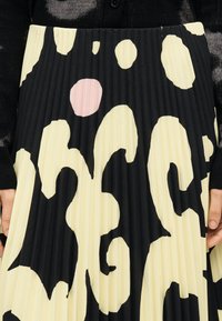 Πλισέ φούστα με μαύρη βάση και μεγάλα κίτρινα και ροζ αφηρημένα σχήματα. Η υφή είναι λεία με κάθετες ραβδώσεις.