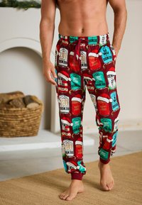 Red pajama pants with a festive pattern featuring beverage labels and Santa hats. Made of soft fabric, with an elastic waistband and drawstring.