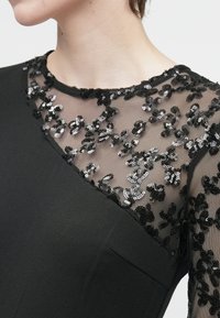 Must mustre mustriga, läbipaistva võrkpaisu ja varrukatega, kaunistatud mustade ja hõbedaste sädelevate lillemusteritega.