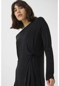 Black long-sleeve dress featuring a twisted knot detail on the side, made from soft, smooth fabric with a relaxed fit.