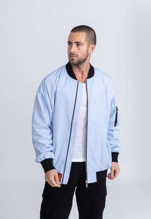 Lichtblauwe bomberjack van gladde stof, met een zwarte rits en boorden, zijzakken en een oranje label op de zoom.