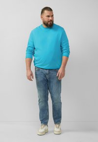Hellblaues Sweatshirt mit Rundhalsausschnitt, kombiniert mit hellblauen Jeans und weißen Sneakers. Der Stoff sieht weich und glatt aus.