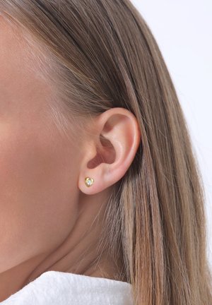 Boucles d'oreilles clous en forme de cœur en or, ornées d'une petite pierre précieuse transparente au centre, sur un fond neutre.