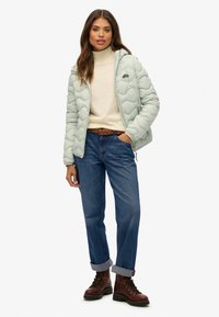 Lichtgroene gewatteerde jas met een capuchon, beige coltrui, blauwe jeans en brown veterschoenen.