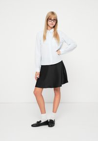 Svijetloplava, dugih rukava, prugasta košulja sa dugim rukavima uparena s crnom, A-linijom suknjom. Crne cipele i bijele čarape upotpunjuju odjevnu kombinaciju.