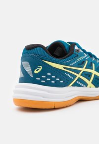 Tyrkysová sportovní bota s černými akcenty, žlutými detaily a bílou a oranžovou podrážkou. Mřížková textura a trojúhelníkový vzor na bocích.