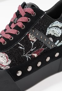 Svarta sneakers med broderad blommönster i burgundy och vitt. Texturerad mocka överdel, svart gummisula och metallisk hårdvara.