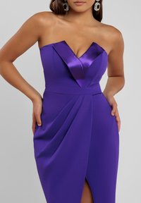 Violetti olkaimeton mekko, jossa on pleatattu etuosan muotoilu, satiinikoristeet ja reiden korkeudelle ulottuva halkio. Sileä pinta ja tiukka siluetti.