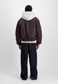 Lila satin bomberjacka med grå huva, med ribbat nederkant och ärmslut, bärs över en grå sweatshirt och mörk denim byxor med vida ben.