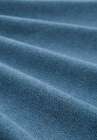 Blauer Stoff mit einer glatten Textur und sichtbarem Gewebe. Das Material hat einen leichten Glanz und ist in sanften, gewellten Falten drapiert.