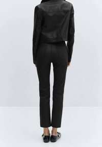 Giubbotto in pelle nera corta abbinato a pantaloni neri slim fit. L'outfit presenta una texture liscia e un design su misura. Scarpe nere flat completano il look.