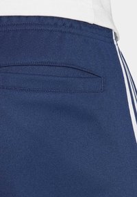 Mørkeblå shorts lavet af åndbart stof har en baglomme med en skjult lukning og hvide sidestriber langs sømmene.