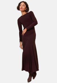 Rochie lungă, ajustată, de culoare burgundă închisă, cu mâneci lungi și decolteu rotund. Are o evazare subtilă la tiv și mici embellismente la umăr.