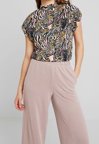 Haut noir avec un imprimé animalier multicolore, manches courtes chauve-souris, associé à un pantalon large rose clair en tissu doux.