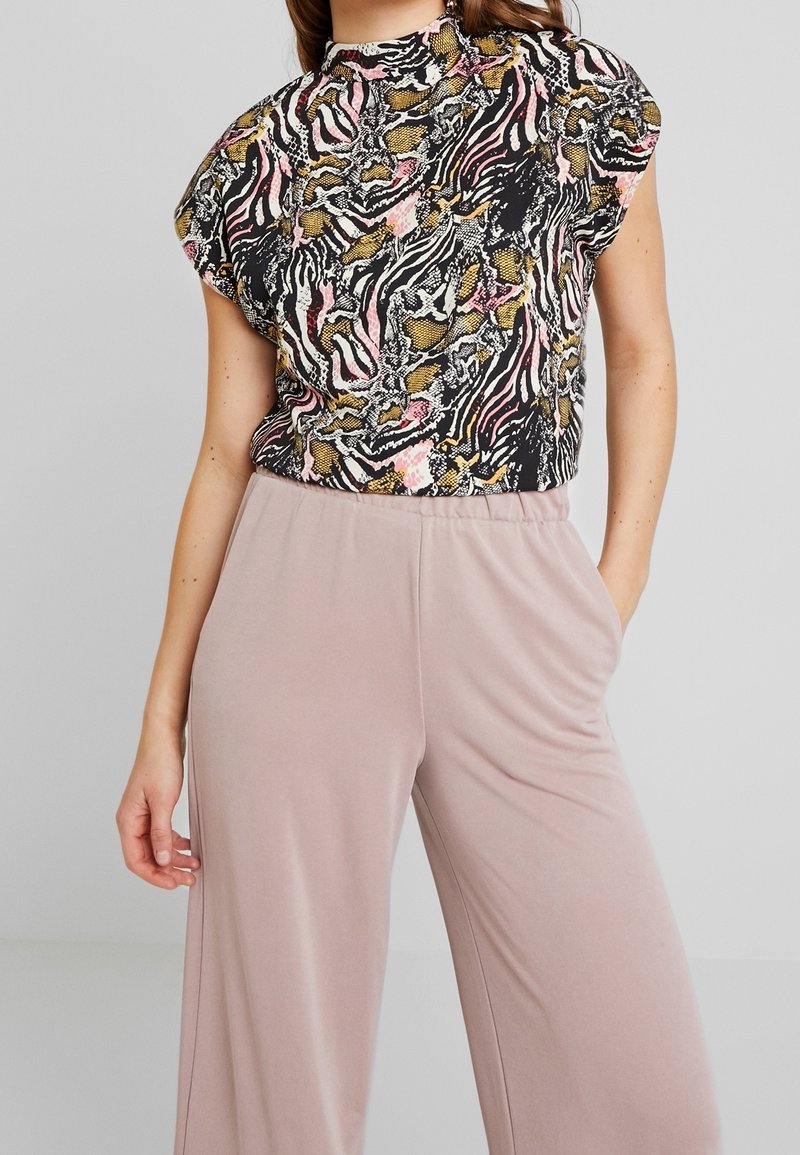 Haut noir avec un imprimé animalier multicolore, manches courtes chauve-souris, associé à un pantalon large rose clair en tissu doux.