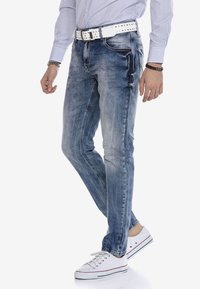Blauwe denim jeans met een slim fit, met een vervaagde afwerking, witte stiksels, voorzakken en een witte studsriem. Gecombineerd met witte sneakers.