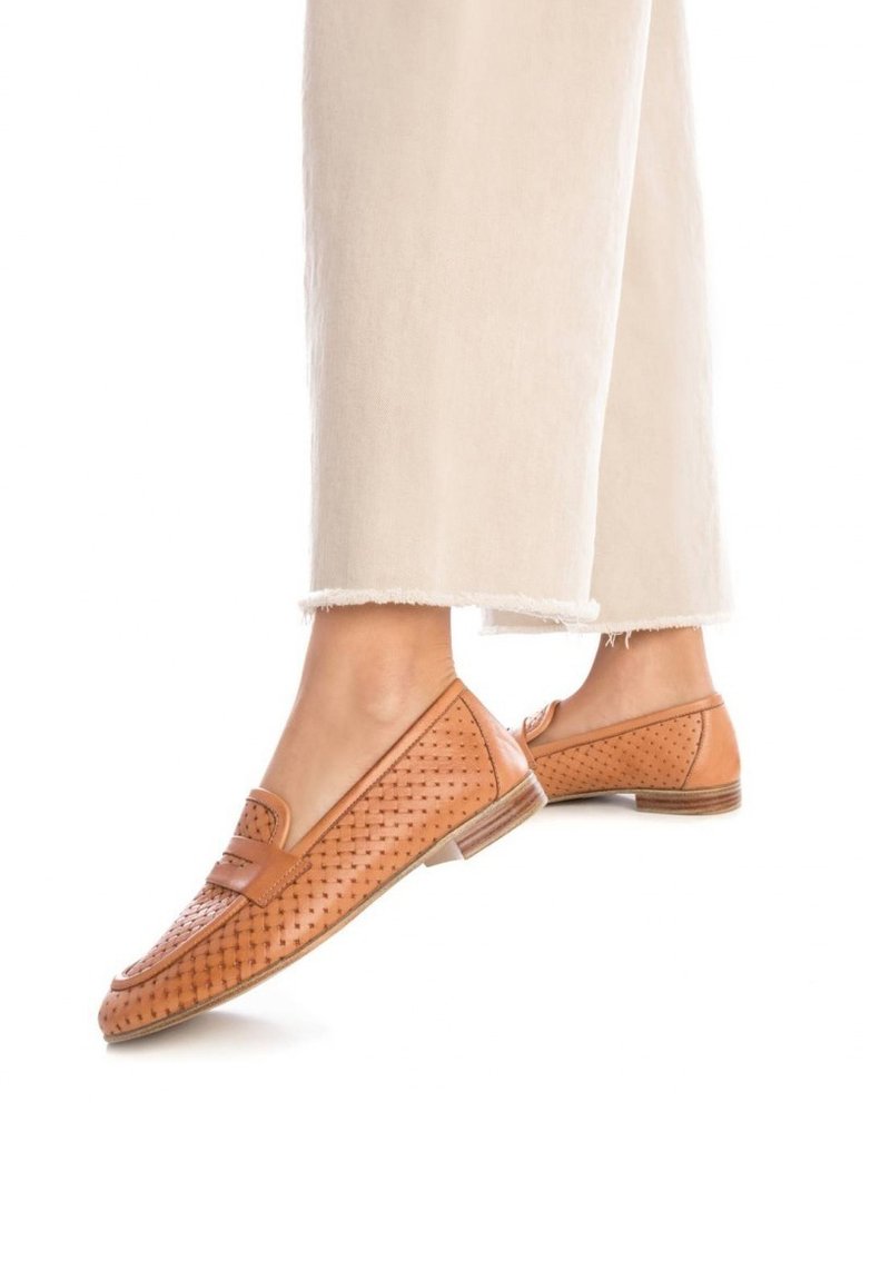 Mocasines de cuero marrón claro con textura trenzada y un pequeño tacón, que presentan una punta redondeada y detalles cosidos, combinados con pantalones de color claro.