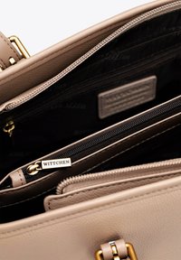 Borsa a mano in pelle beige con più scomparti interni, hardware dorato e tasche con zip. Progettata con una finitura testurizzata.