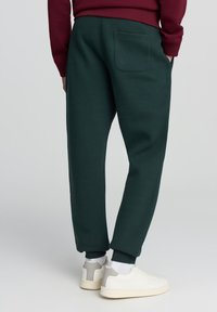 Zielone dresowe spodnie o luźnym kroju, z jedną tylną kieszenią i elastycznymi mankietami, zestawione z białymi sneakersami.