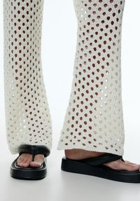 Zwarte platformflip-flops met een kenmerkende dikke band, gecombineerd met off-white gebreide broeken met een ademend ontwerp met open gaten.