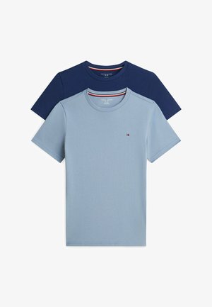 Garçon debout pieds nus, portant une chemise bleu à manches courtes et un pantalon de pyjama bleu clair à motifs, sur un fond blanc.