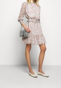 Sukienka w kwiaty z długimi rękawami, marszczoną talią i falbaną na dole; zdobiona różowymi i pomarańczowymi kwiatami na jasnym tle. Srebrna pikowana torebka i baleriny.