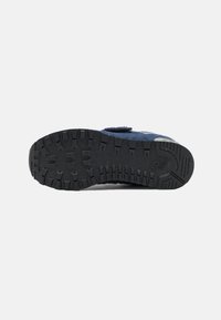 Soulier en suede bleu avec une semelle en caoutchouc noir texturé présentant des rainures profondes pour l'adhérence et une sangle Velcro pour un ajustement sécurisé.