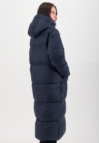 Lange marineblauwe pufferjas met capuchon, met een geborduurd ontwerp en ruime pasvorm. Glad, waterafstotend materiaal met zijzakken.