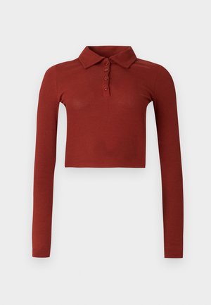 Polo à manches longues recadré en tissu côtelé rouge rouille, avec col et patte de boutonnage à six boutons sur le devant.