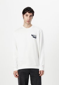 Hvid langærmet sweatshirt med et mørkeblåt "Tommy Jeans" logo på brystet og ribbede manchetter. Glat stof og afslappet pasform.