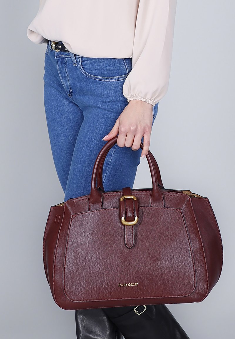 Burgundin värinen nahkalaukku, jossa on kaksi kahvaa, kultasävyisiä metalliosia, jämäkkä muotoilu ja teksturoitu pinta; varustettu soljella.