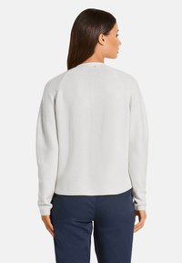 Witte trui met een ronde hals en lange mouwen, met een geweven patroon. De achterkant is iets langer en heeft geribbelde boorden.