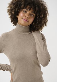 Maglione beige a collo alto con coste, realizzato in materiale morbido, design aderente, maniche lunghe e colletto alto. Nessun motivo o accento distintivo.