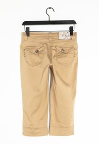 Beiga cropped-byxor upplagda på en svart galge. Har två bakfickor med knappstängningar och dekorativa nitar längs den vänstra fickan.