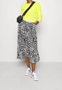 Neon żółty sweter z dzianiny, midi spódnica w czarno-białą zebra, oraz białe sneakersy z szarymi akcentami i różowym detalem.