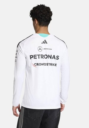 Hombre con cabello rizado de espaldas, vistiendo una camisa blanca de manga larga con los logos de Mercedes AMG Petronas y CrowdStrike en la parte posterior.